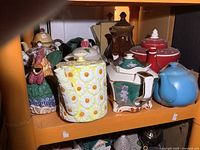 Shelf holding 11 assorted teapots of varying sizes and styles including floral, colorful, and wooden types.