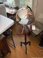 Photo showing the globe on the oval tilt top table in room setting with windows in background.