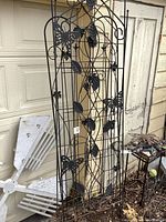 Full view of black metal trellis panel with butterfly and leaf decorative elements standing against a garage door.