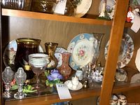 Shelf displaying an assortment of glass and porcelain items including salt and pepper shakers, mini vases, plates with floral and figure decor, and small collectibles.