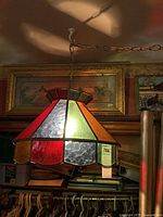 Photo showing the stained glass hanging swag lamp lit, featuring red, green, and textured glass panels and the chain from which it hangs.