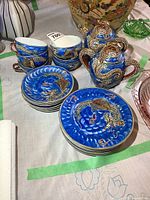 Full view of tea set including stacked cups, saucers, snack plates, and the creamer and sugar bowl with detailed dragon design.