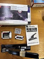 Photo showing the Swingline 39T heavy duty stapler in box, two boxes of heavy duty staples, and the stapler operating instructions on a wooden surface.