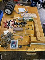 Overview of assorted hardware and workshop accessories including clamps, wheels, storage containers, and various fasteners laid out on a wooden table.