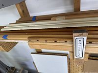 Assorted wood and plastic moldings placed on a wooden rack showing natural wood grain and painted white pieces