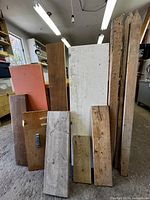 Photo showing several assorted wood pieces leaning against each other including a large white painted board, natural wood planks with different finishes, and narrow beams.