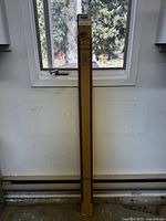 Full length photo of boxed burgundy mini blind standing vertically against white wall beneath window, showing overall condition and packaging.