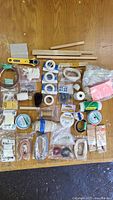 Top-down photo of all bookbinding supplies spread out showing threads, tapes, rotary cutter, wooden tools, beeswax and other small items.