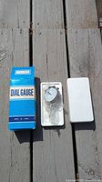 Photo showing dial gauge in original packaging with a blue and white labeled box and white foam insert.