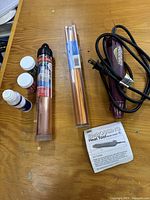 Photo showing Marvy Embossing Heat Tool Model 2500 with black power cord, a copper metallic foil roll in clear packaging, three jars of embossing powder in different colors, and instruction sheet.
