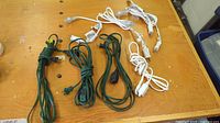Top-down photo showing six coiled extension cords, three white and three green, laid out on a wood surface.