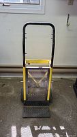 Front view of heavy duty hand truck showing yellow frame, black handle, metal mesh back, and footplate.