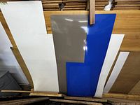 Five laminate boards in various colors and sizes arranged leaning against a wooden surface, showing white, tan, blue, and dark brown colors.