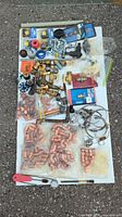 Top-down view of a broad assortment of copper fittings, brass fittings, valves, various plumbing hardware and plastic fittings all laid out on a white cloth or surface outdoors with grey stone ground below.