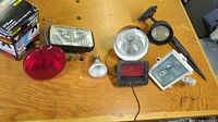 Photo showing layout of various lighting bulbs and fixtures including red bulb, rectangular fixtures, spotlight, and garden stake light on wooden surface.