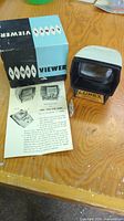 Full view of Lumex CAT 21102 slide viewer with original box and instruction manual on wooden table.