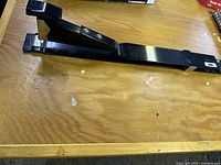 Full length view of the manual heavy-duty book stapler with long black metal arm on wooden surface.