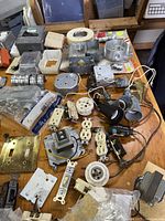 Photo of a variety of electrical components including switches, receptacles, electrical boxes, timers, conduit fittings, and connectors on a wooden surface showing condition and variety of vintage and new items.