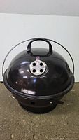 Front view of the black round kettle portable charcoal grill with top vent and carry handle on lid.