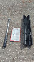 Torque wrench, case, and instruction sheet laid out outdoors on asphalt ground