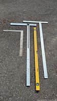 Photo showing full set of measuring squares and leveler laid out on gravel surface.