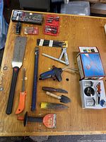Full layout shot of tools on wooden table showing hand saws, garden trowels, Bernzomatic torch, Aerograph spray tool box, hand tools, and blades