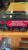 Front and top view of the rectangular black and red MotoMaster battery charger showing label details and controls on the front panel.