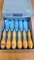 Photo of the full set of six Sorby wood carving tools in a labeled box showing the wooden handles and various blade shapes.