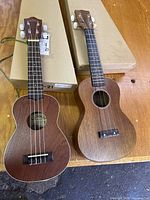 Top view of two ukuleles side by side showing the Lanikai LU-21 with white binding and the Classic Lowa CL-300M with a plain wooden finish.