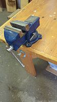 Side angle view of vintage bench vice clamped to wooden workbench showing general condition and mounting.