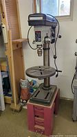 Front view of Rexon drill press on red stand showing table, column and head assembly
