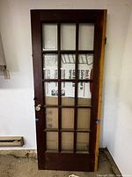 Full front view of the vintage wooden French door with 15 glass panes and glass knob, showing the reddish-brown wood frame and intact panes.