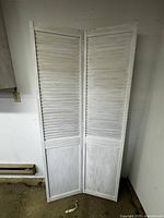 Full view of white wooden bifold door standing upright, showing two connected panels with louvered design and solid bottom sections.