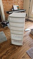 White 6-drawer plastic organizer standing on a wood floor with a keyboard and some furniture in background. Drawers appear transparent