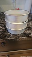 Stack of three silver metal round cake pans, 6-inch diameter each, stacked on countertop.