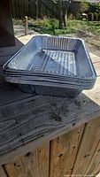 Stack of 8 rectangular aluminum foil pans on wooden surface outdoors, showing side and top edges stacked flat.