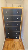 Full view of the tall 6-drawer chest with natural wood frame and black drawer fronts, showing metal knobs.