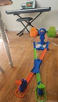 Long view of the assembled colorful Hot Wheels track set on a wooden floor with two towers and track pieces in orange, blue, and green.