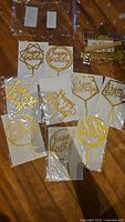 Photo of 10 packaged Happy Birthday cake toppers in various shapes and gold color with white background laid out on floor