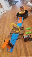 Full view of Hot Wheels monster trucks playset with carrying case, launcher ramp, loop, green ramps, and monster truck vehicle arranged on wooden floor.