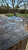 Clear glass dome placed on wood surface outdoors, showing dome shape with knob handle on top