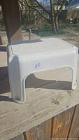 Side view of white Rubbermaid plastic step stool on wooden surface in daylight.