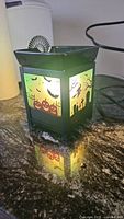 Black ceramic Scentsy wax warmer lit up indoors, showing Halloween-themed cutout scenes with bats, pumpkins, witches, and graveyard on sides