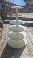 Full view of the assembled 5-tier white plastic cake stand outdoors on wooden board.