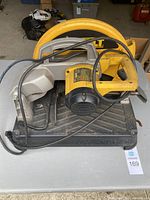 Overview of yellow and black DeWalt chop saw showing handle, motor, and base, with cord resting over saw body.