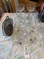 Overview of the 8 Mikasa Romaine glasses with gold rim and metal wine holder basket on white surface.