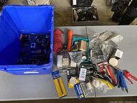 Wide shot of table showing blue bin filled with various small metal parts and multiple coiled hoses, air guns, and packaged accessories arranged on table