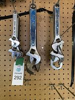 Three adjustable wrenches hanging on pegboard, showing brand marks and size.