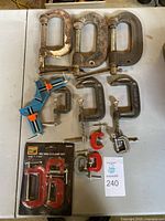 All clamps laid out on a table including large metal C-clamps, quick grip clamps, smaller metal C-clamps, and new boxed mini clamps.