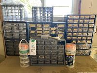 Front view of seven plastic organizers filled with assorted screws and nails, showing multiple small clear drawers stacked together in front of a window.